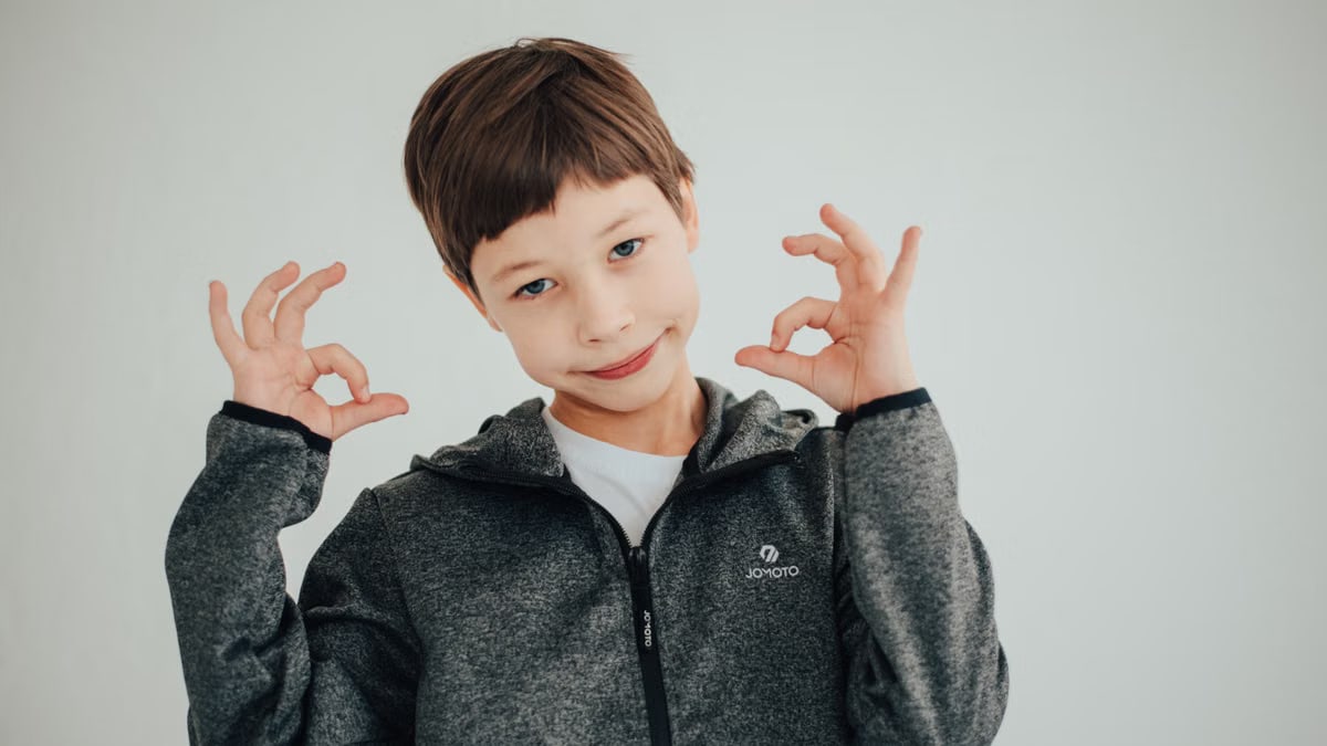 A young boy happily posing with OK gestures on a white background.